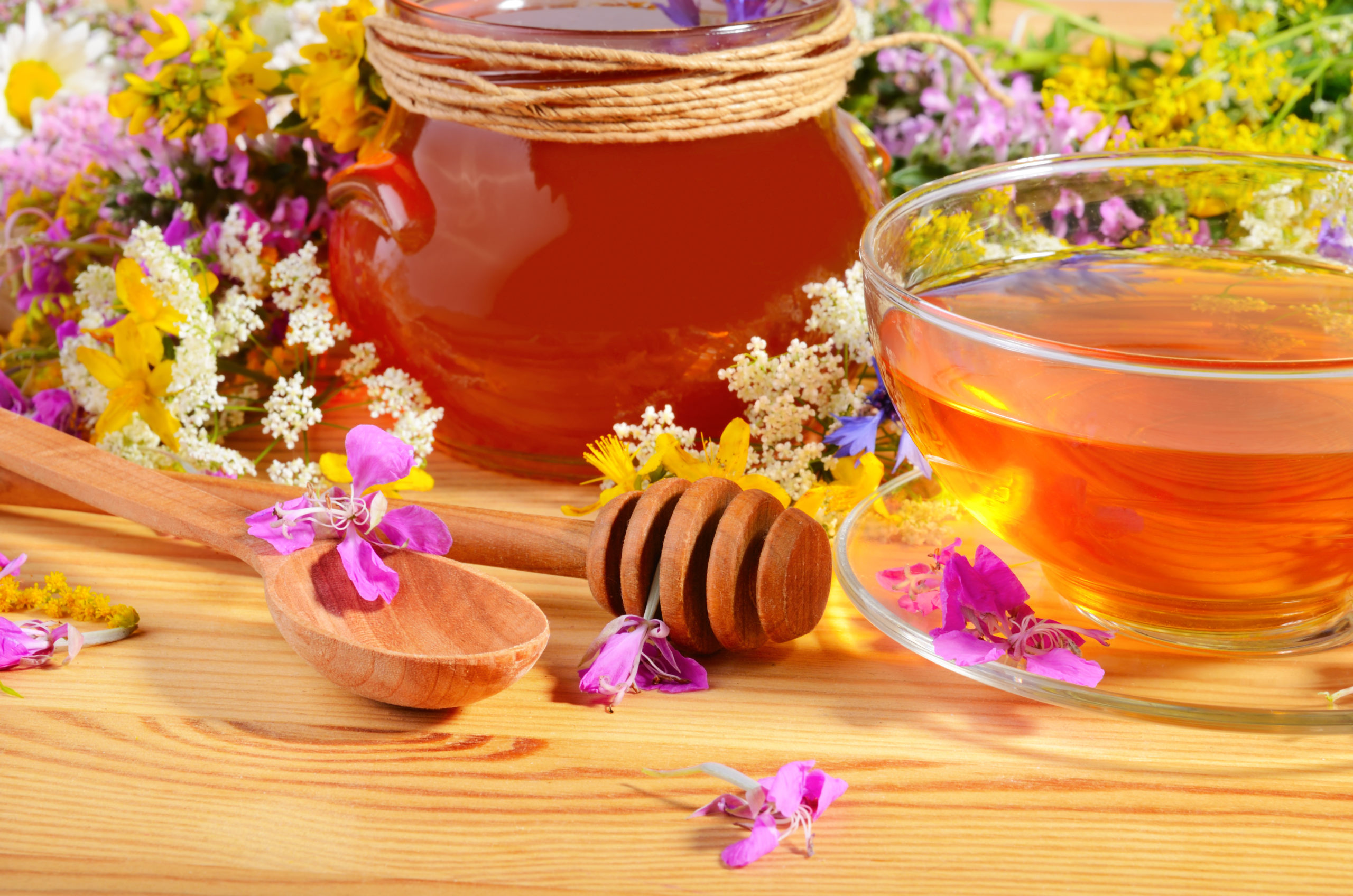 Tea in cup and spoons for honey on wooden table with flowers